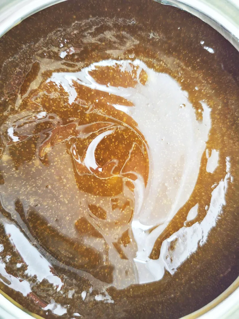Amber open-gear lubricant swirled across the surface of an open pail.